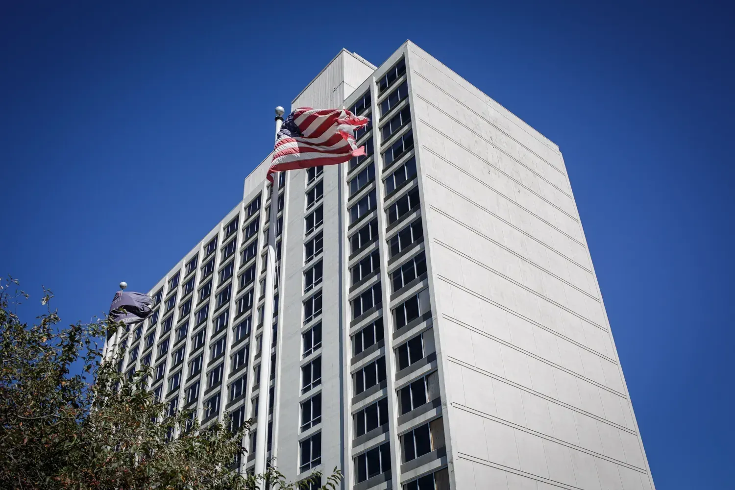 A tall mid-century apartment tower against a clear sky, a United States flag flying from its roof.