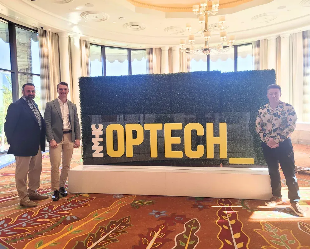 Three Lavanda team members standing beside the NMHC OPTECH sign.