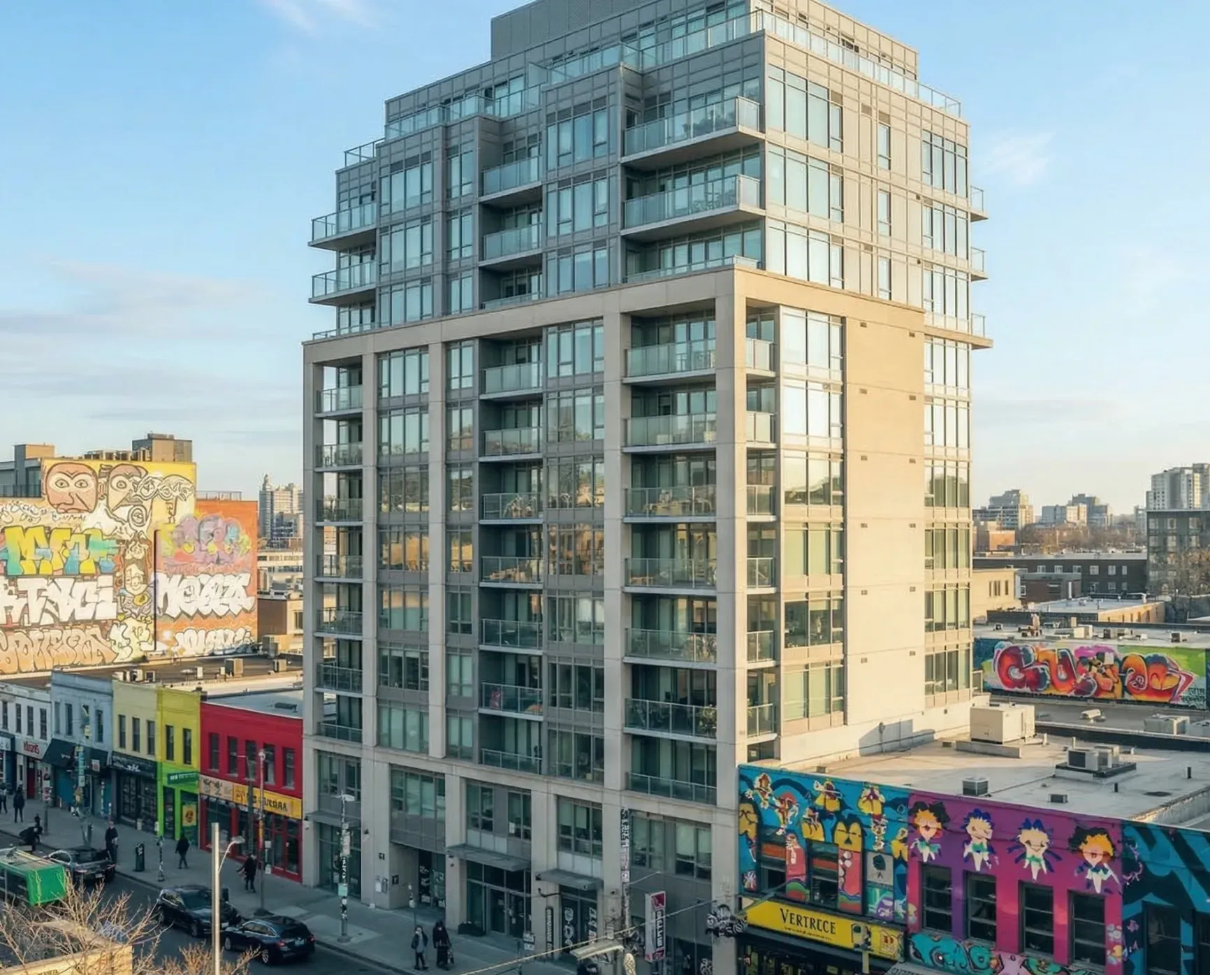 A mid-rise apartment block on a corner, the buildings opposite covered in bright murals.